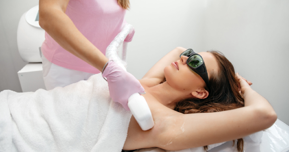 Woman receiving laser hair removal reduction on underarm area while lying on a clinic bed, wearing protective eyewear and attended by a technician in gloves in Laredo, TX